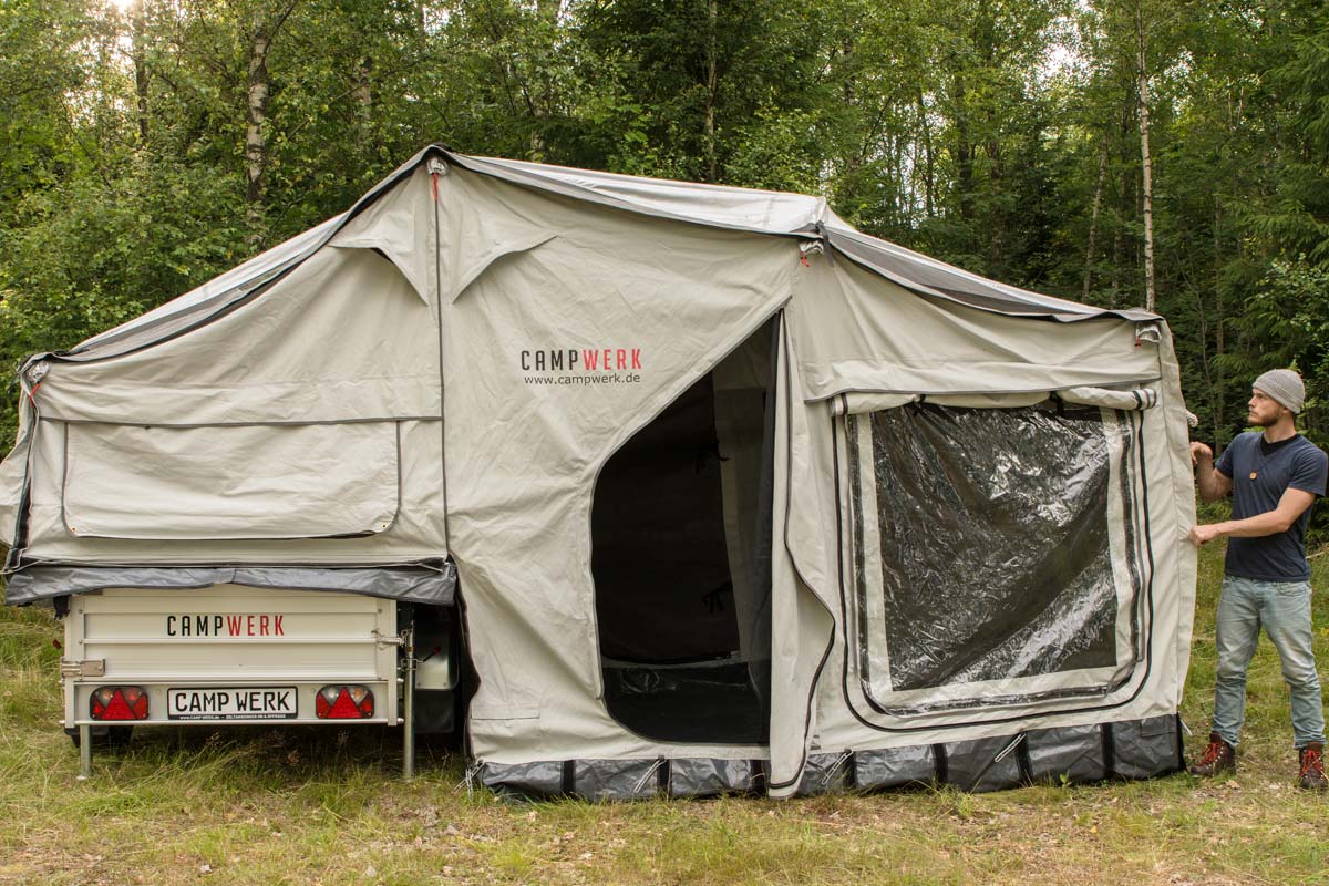 CAMPWERK Dachzelt-Anhänger mit großem Vorzelt und Person beim Aufbau im Grünen