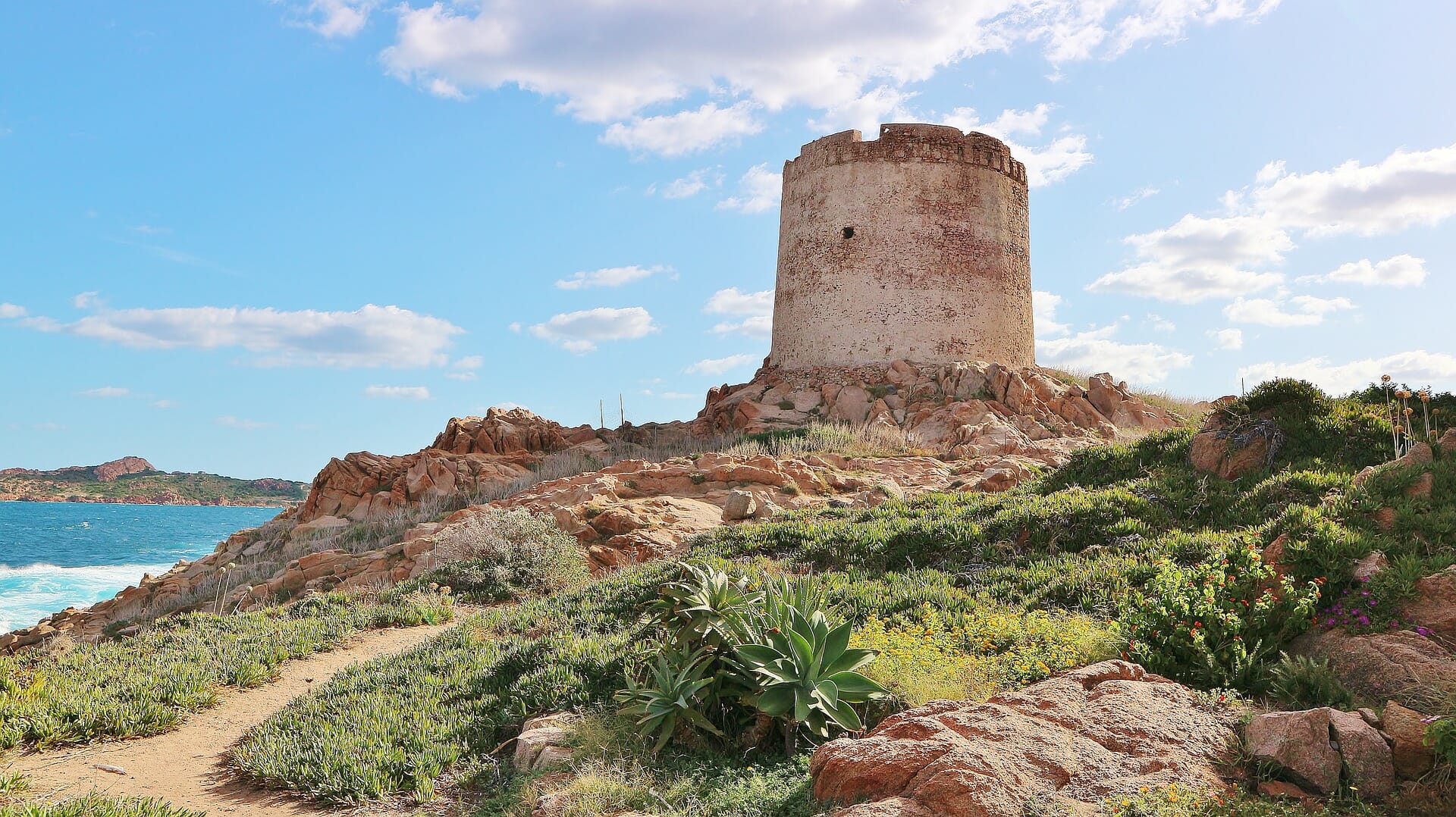 La ruina de una torre se alza sobre una colina y en el fondo se puede ver el mar