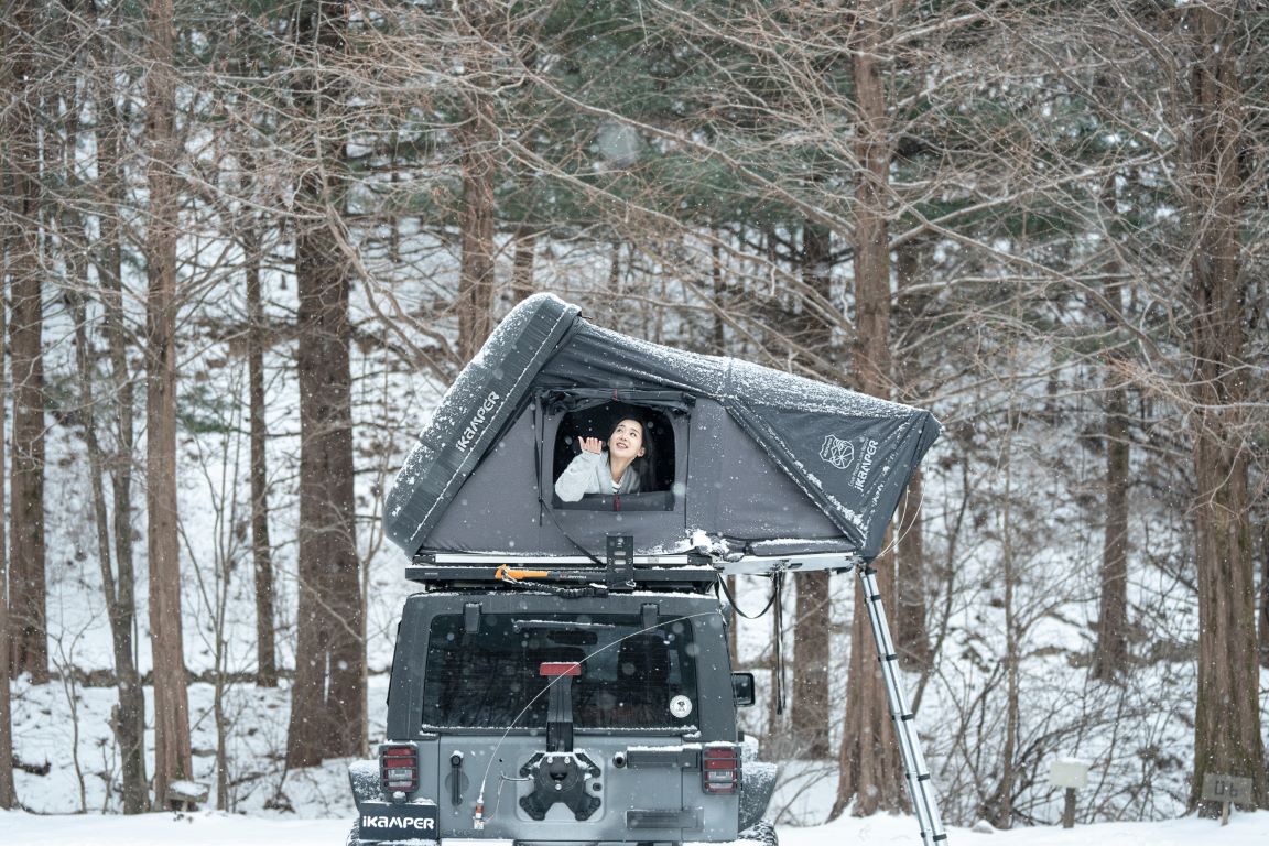 Una mujer disfruta de la nieve alrededor de su tienda de techo Skycamp en invierno