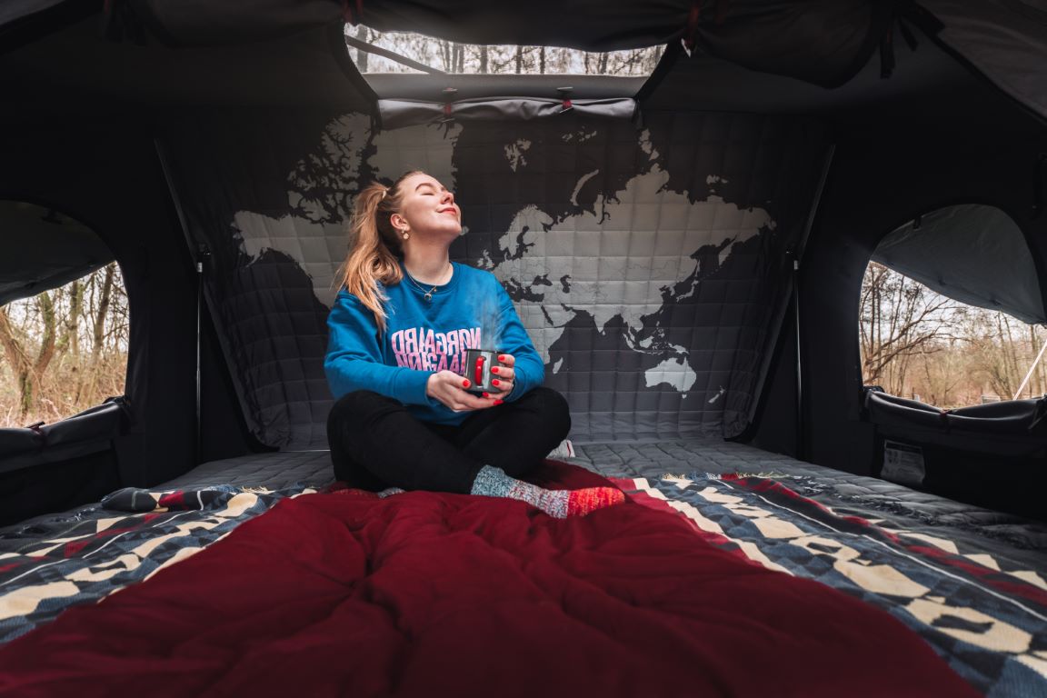 Una mujer se relaja con una taza de té en su tienda de techo Toyota Hilux