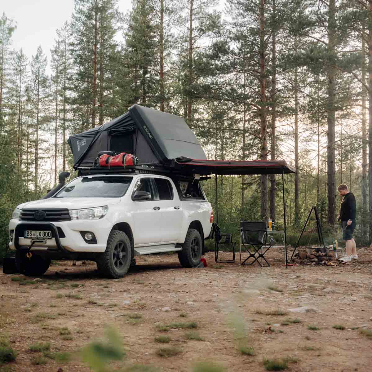 Un hombre acampa con su camioneta pickup con tienda de techo y toldo en el bosque