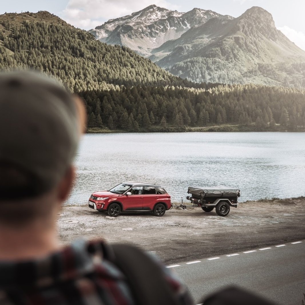 Persona mirando un coche con un remolque tienda desenganchado en el lago